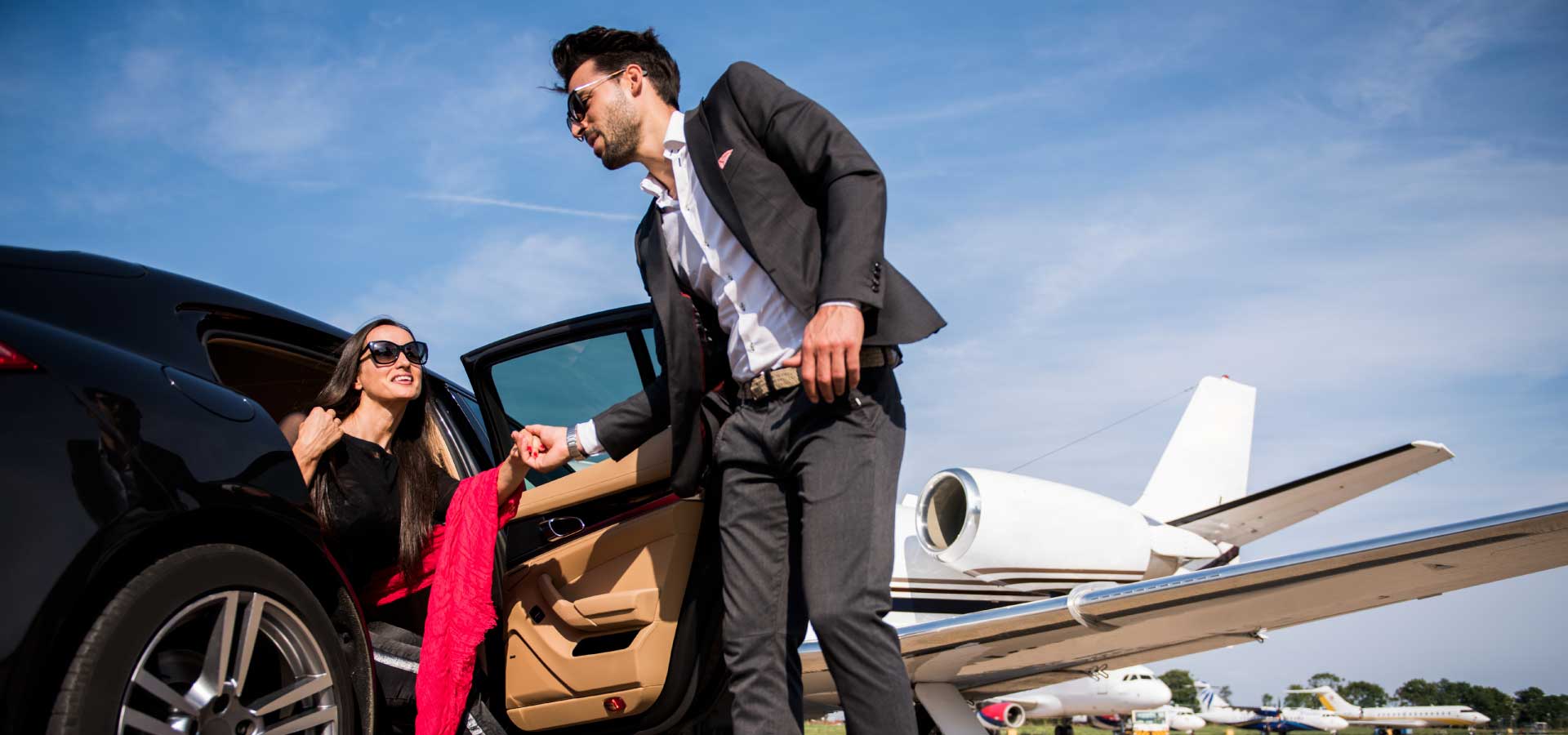 Man helping woman out of taxi in front of business jet